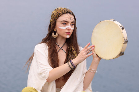Beautiful shaman woman with tambourine performing ritual outdoorsの写真素材