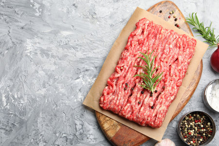 Raw minced meat with rosemary and spices on gray textured table, flat lay. Space for text
