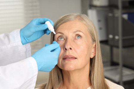 Doctor putting drops into woman's eye indoors, closeup