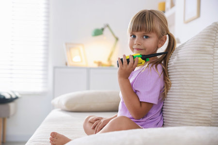 Little girl playing with walkie talkie toy on sofa at home, space for textの写真素材
