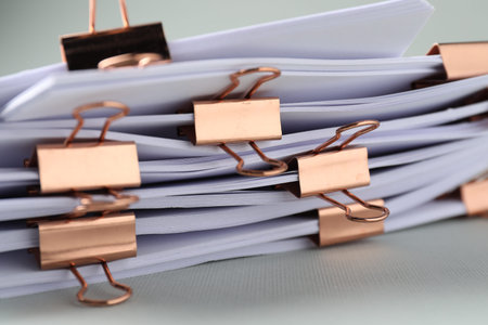 Many documents with binder clips on light gray background, closeup