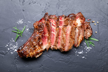 Tasty cut beef steak, salt, peppercorns and rosemary on black table, flat layの写真素材