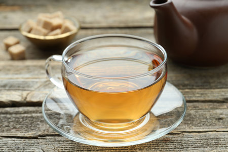Aromatic black tea in glass cup, brown sugar and teapot on wooden table, closeupの写真素材