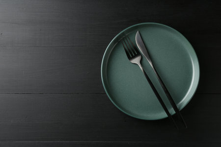 Clean ceramic plate and cutlery on black wooden table, top view. Space for textの写真素材