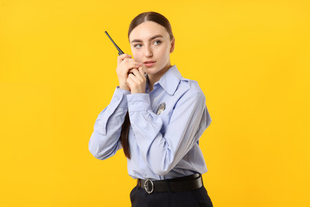 Young policewoman in uniform with walkie talkie on yellow backgroundの写真素材