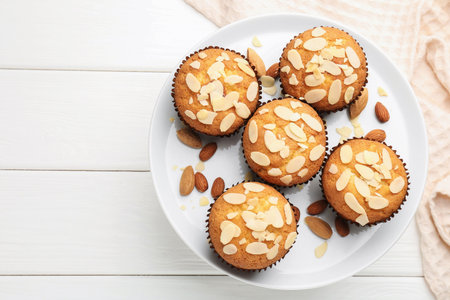 Tasty muffins with almond flakes and nuts on white wooden table, top view. Space for textの写真素材