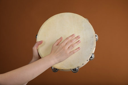 Woman playing tambourine on brown background, closeupの写真素材