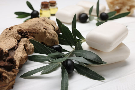 Handmade soap bars, olives, green leaves, essential oils and loofah on white wooden table, closeupの写真素材