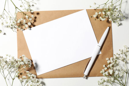 Blank card, envelope, pen and beautiful flowers on white background, flat layの写真素材