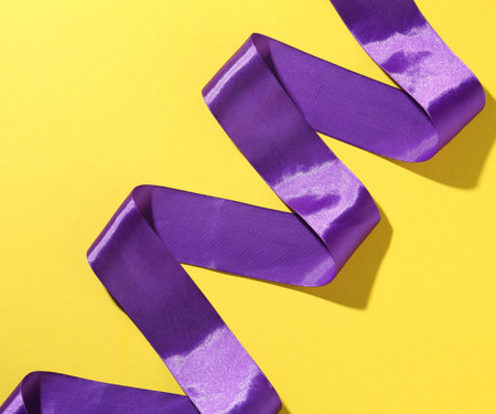 Beautiful violet ribbon on yellow background, top viewの写真素材
