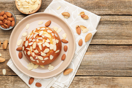 Tasty roll bun with almond flakes and nuts on wooden table, flat lay. Space for textの写真素材