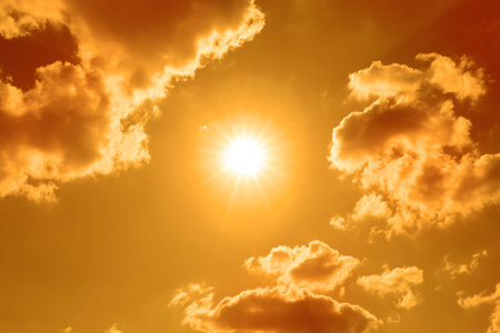 Bright sun and clouds in orange sky during hot summer weather