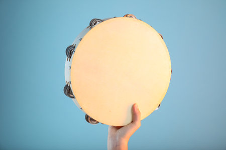 Woman playing tambourine on light blue background, closeupの写真素材