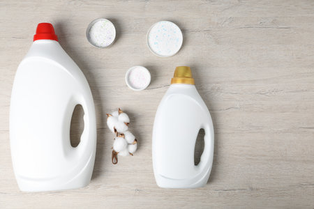 Bottles of fabric softener, washing powder and cotton flowers on wooden table, flat layの写真素材