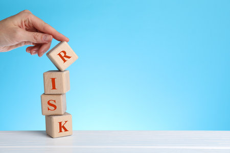 Woman making word Risk of wooden cubes at table against light blue background, closeupの写真素材
