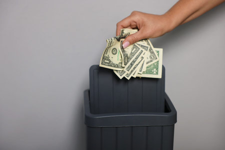 Woman throwing dollar banknotes into trash bin near light wall indoors, closeupの写真素材