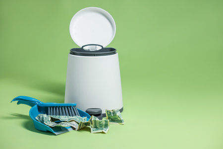 Dollar banknotes, dustpan, broom and trash bin on green background. Space for textの写真素材