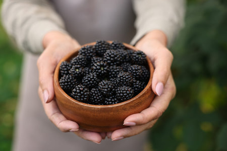 Senior woman holding bowl of ripe blackberries in garden, closeup