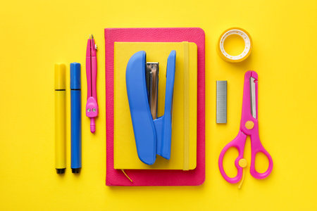 Blue stapler and other stationery on yellow background, flat lay