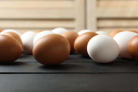 Many raw chicken eggs on black wooden table indoors, closeup