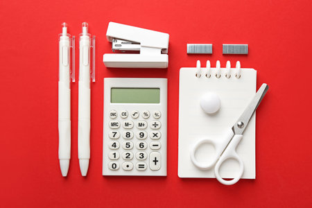 Stapler and other stationery on red background, flat lay