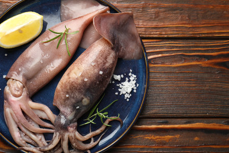 Raw squids, lemon and rosemary on wooden table, top view. Space for textの写真素材