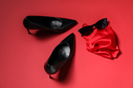 Pair of stylish high heeled shoes, sunglasses and handkerchief on red background, flat layの写真素材