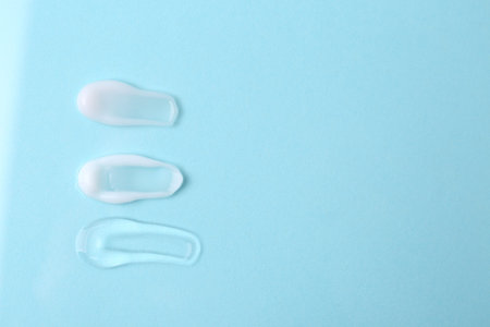 Samples of cosmetic products on light blue background, flat lay. Space for text