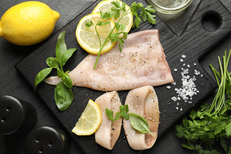 Pieces of raw squid, lemon and herbs on black table, flat layの写真素材
