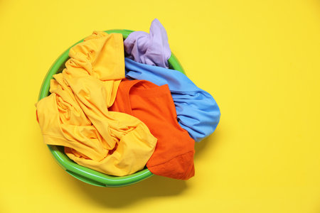 Plastic basin with clothes on yellow background, top view. Space for textの写真素材
