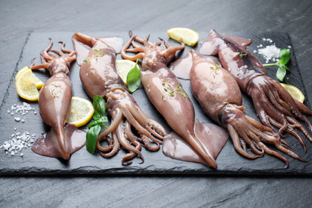 Raw squids, lemon and basil on black table, closeup