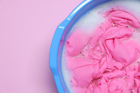 Plastic basin with clothes, water and foam on pink background, top view. Space for textの写真素材