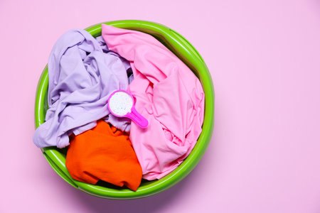 Plastic basin with clothes and washing powder on pink background, top view. Space for textの写真素材