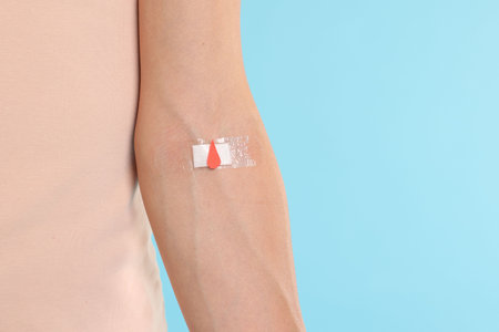 Blood donation. Woman with bandage on arm against light blue background, closeup. Space for textの写真素材