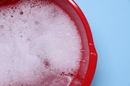 Red plastic basin with water and foam on light blue background, top viewの写真素材