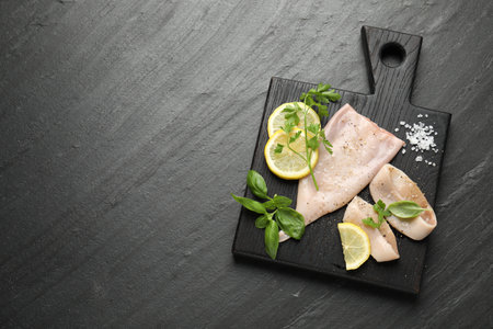 Pieces of raw squid, lemon and herbs on black table, top view. Space for textの写真素材