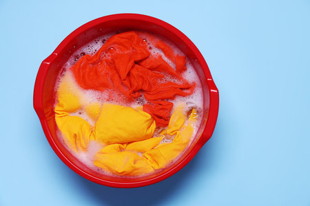 Plastic basin with clothes, water and foam on light blue background, top viewの写真素材