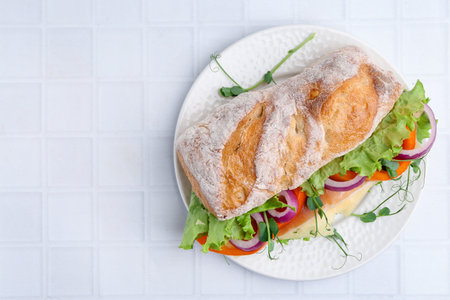 Delicious ciabatta sandwich with prosciutto, cheese and vegetables on white tiled table, top view. Space for textの写真素材