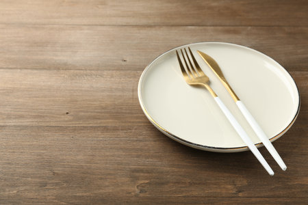 Clean ceramic plate and cutlery on wooden table. Space for textの写真素材