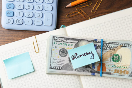 Note with word Alimony, money, notebook, pencil, clips and calculator on wooden table, flat lay