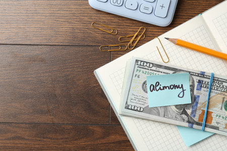 Note with word Alimony, money, notebook, pencil, clips and calculator on wooden table, flat lay. Space for textの写真素材