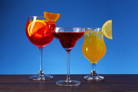 Glasses of tasty cocktails with garnish on wooden table against blue backgroundの写真素材