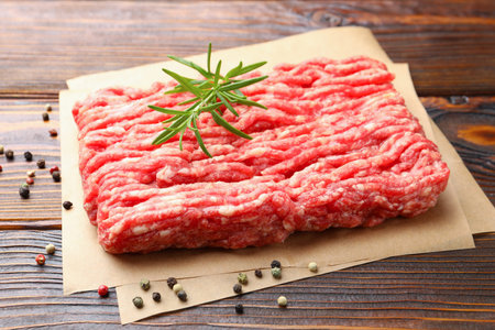 Raw minced meat with rosemary on wooden table, closeup