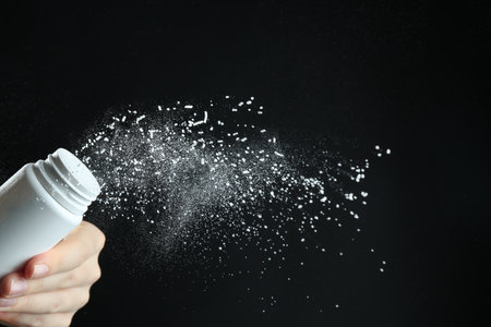 Woman with talcum powder on black background, closeup. Space for textの写真素材