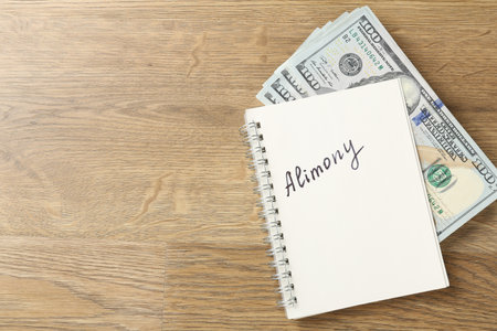 Notebook with word alimony and money on wooden table, top view. Space for textの写真素材