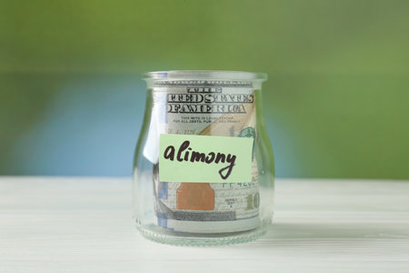 Jar with word Alimony and money on white wooden table against blurred backgroundの写真素材