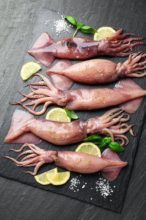 Raw squids, lemon and basil on black table, top viewの写真素材