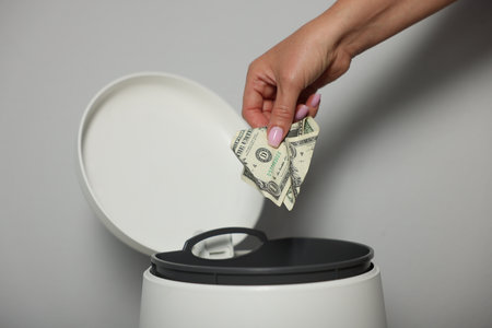 Woman throwing dollar banknotes into trash bin near light wall indoors, closeupの写真素材