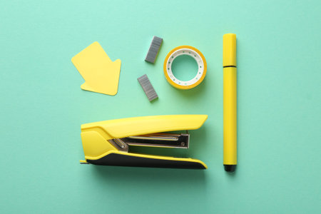 Stapler and other stationery on turquoise background, flat lay