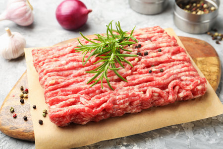 Raw minced meat with rosemary and spices on gray textured table, closeupの写真素材